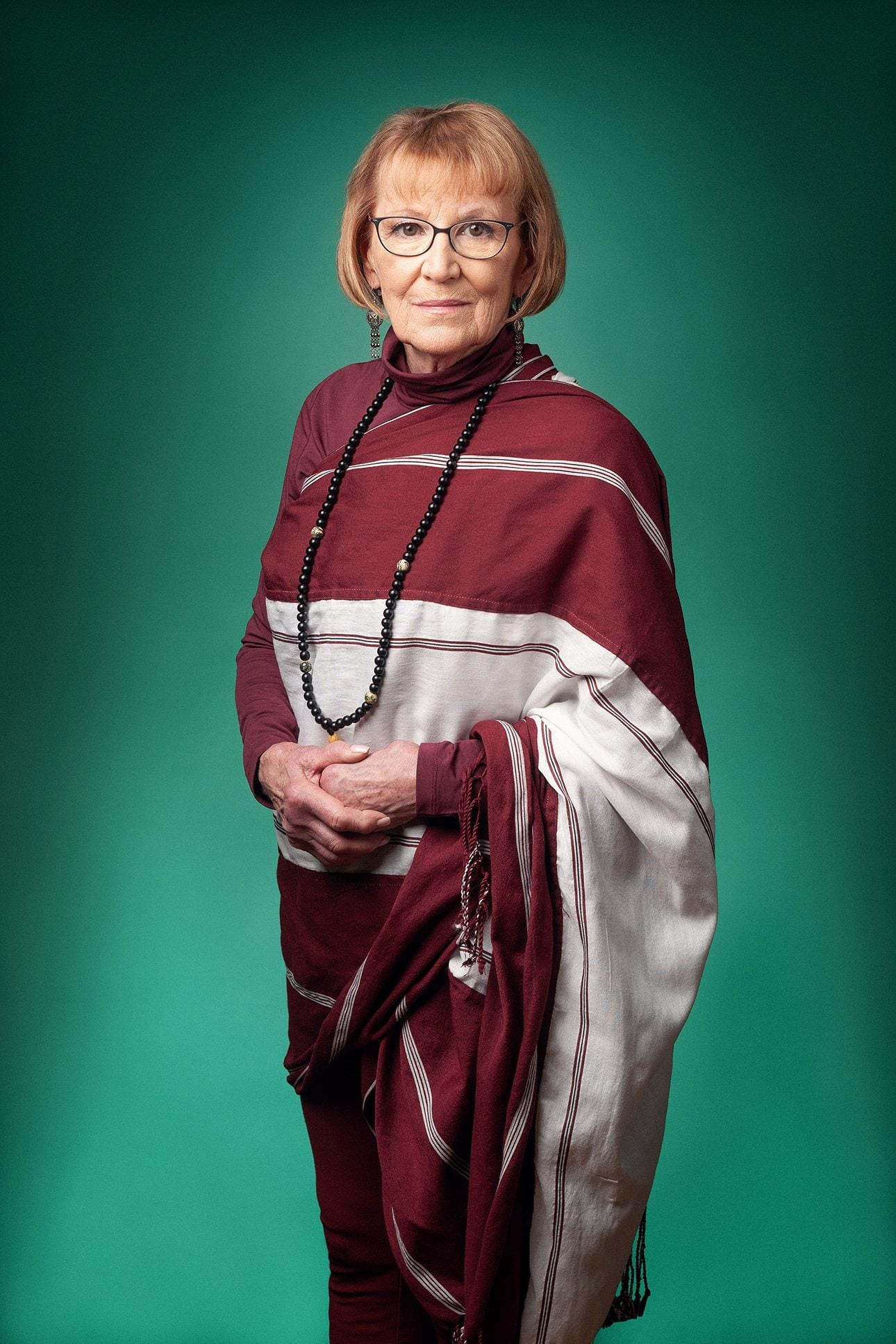 Elderly woman in maroon and white shawl against green background