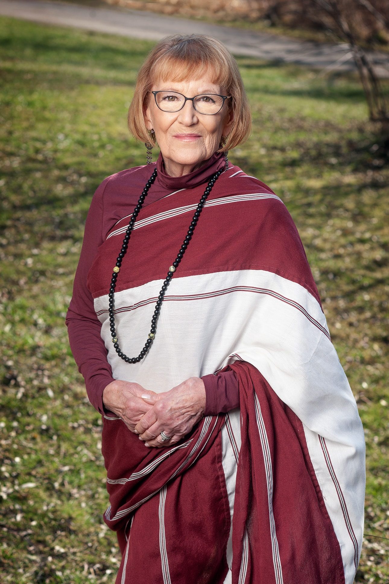 Elderly woman in maroon and white sari stands on grass