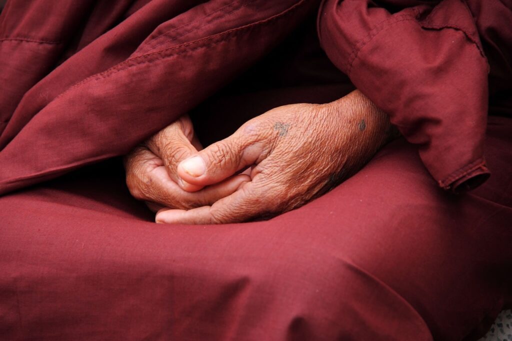 Hands of a person in meditation or prayer, wearing maroon robe