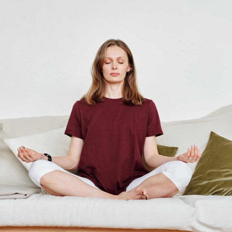 Woman in meditation pose sitting on a sofa