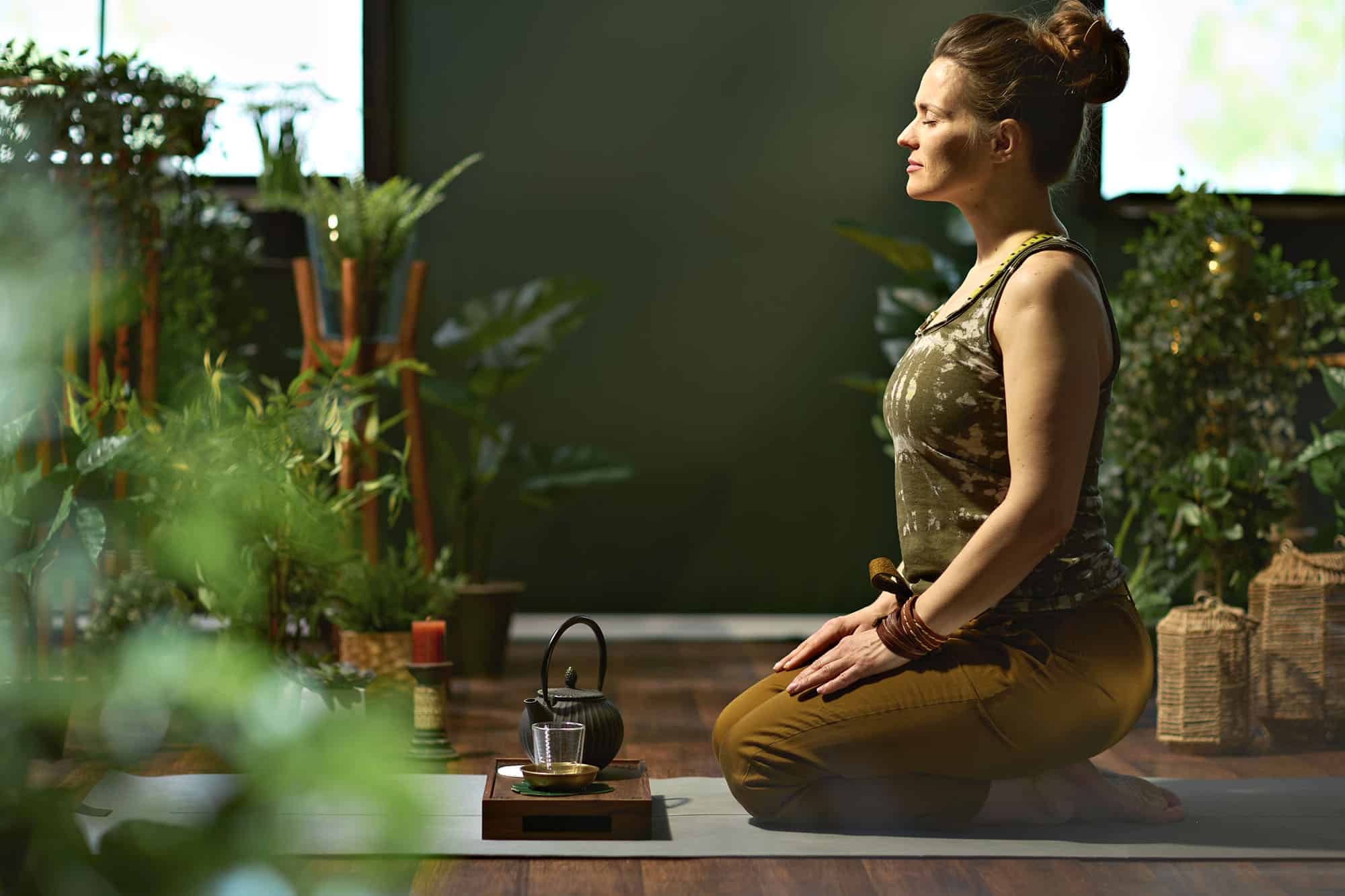 Woman meditating in serene home yoga space surrounded by plants