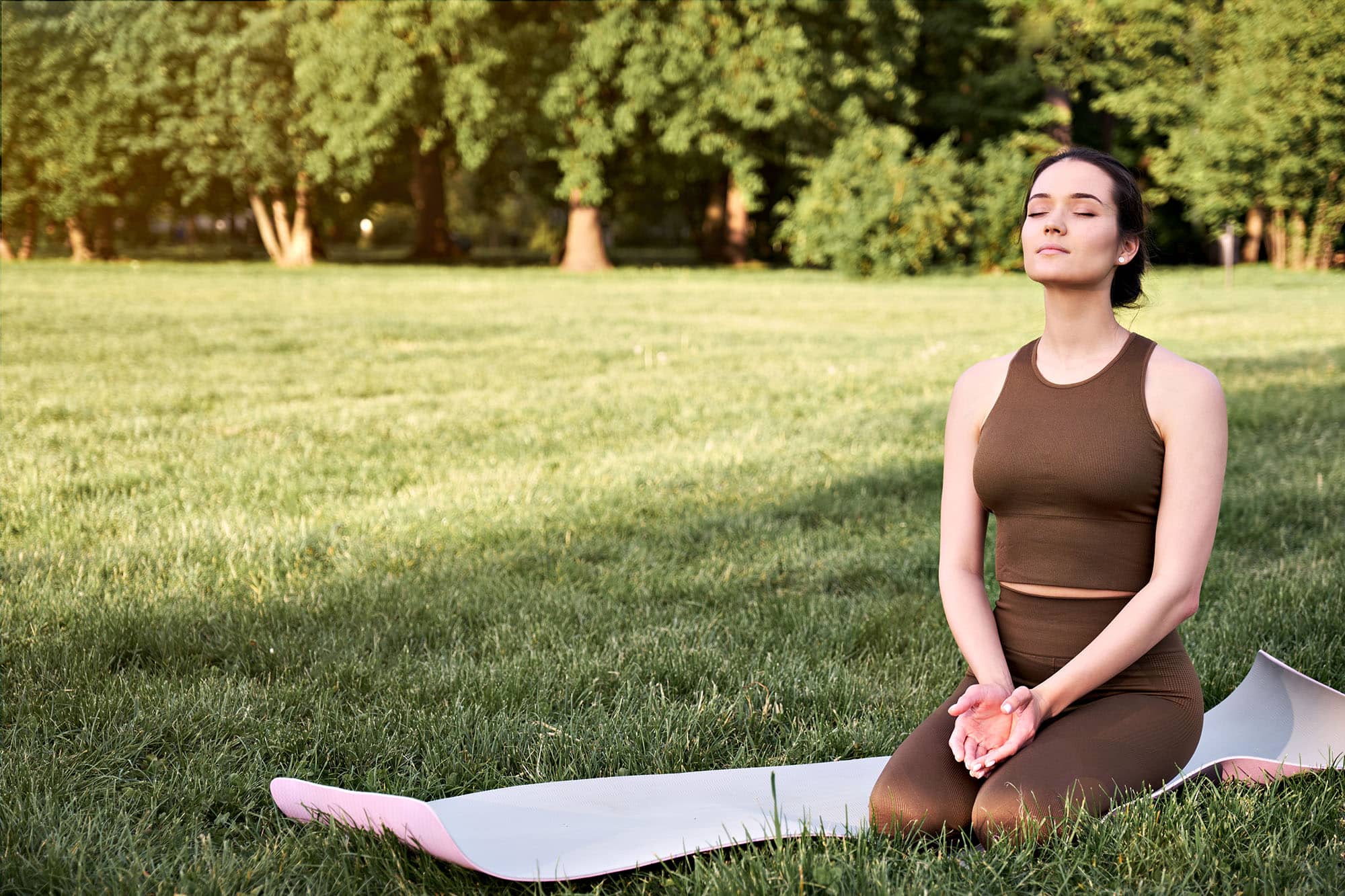 Woman meditating on yoga mat in a sunny park