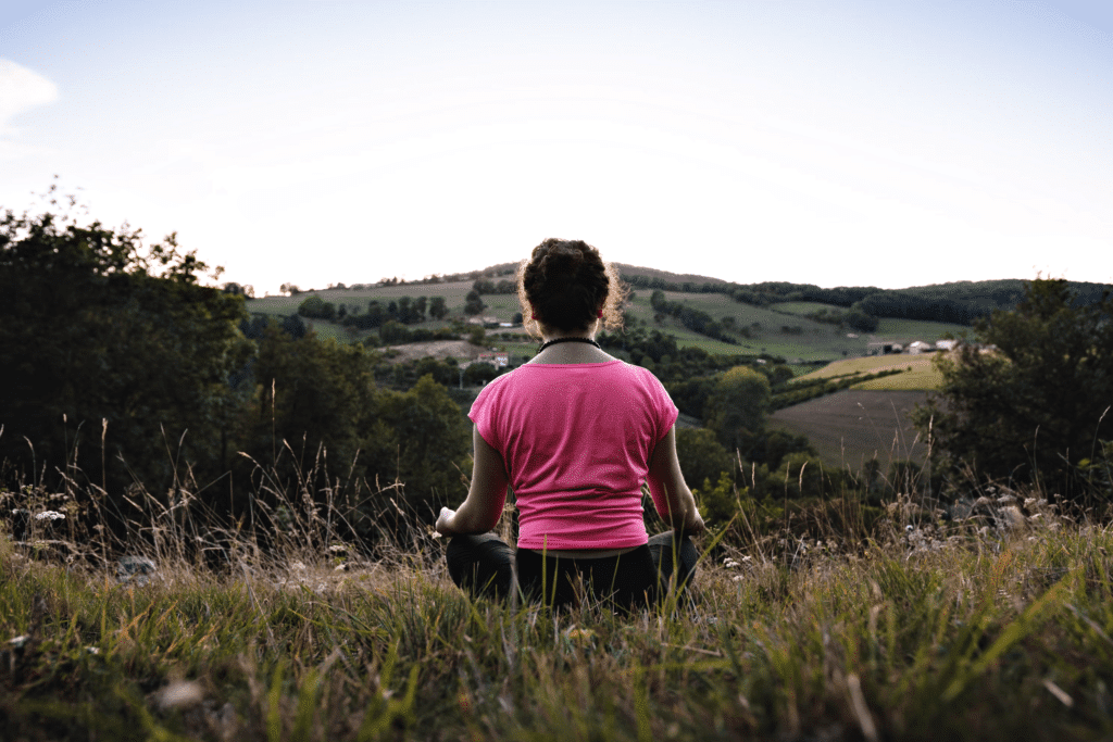 Woman meditating in nature facing picturesque hills at sunset