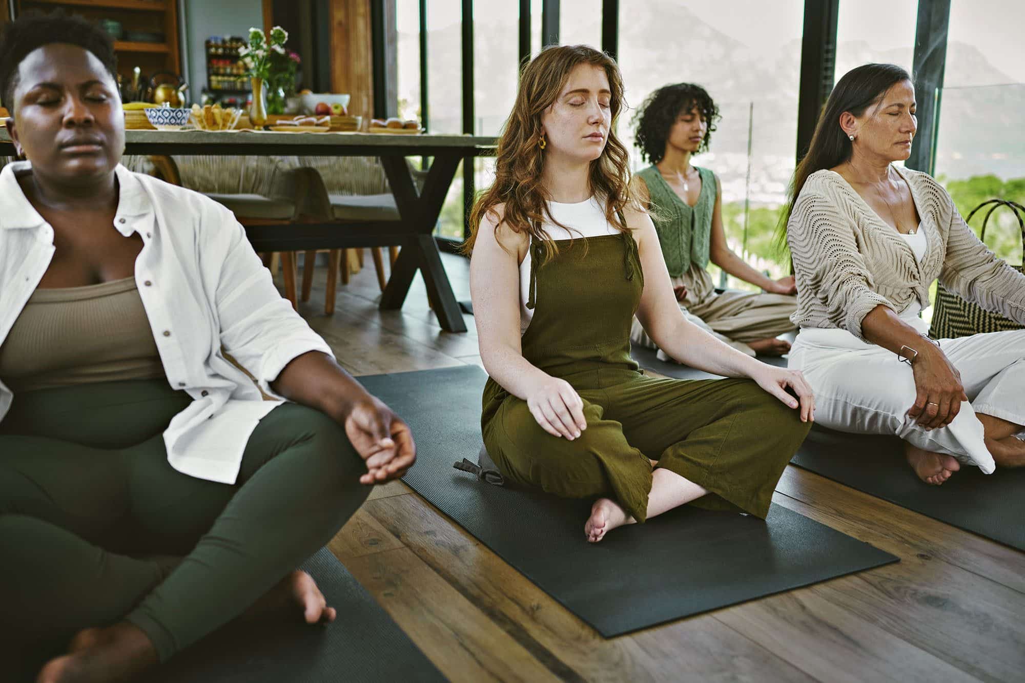 Diverse group meditating in a serene indoor setting with mountains view